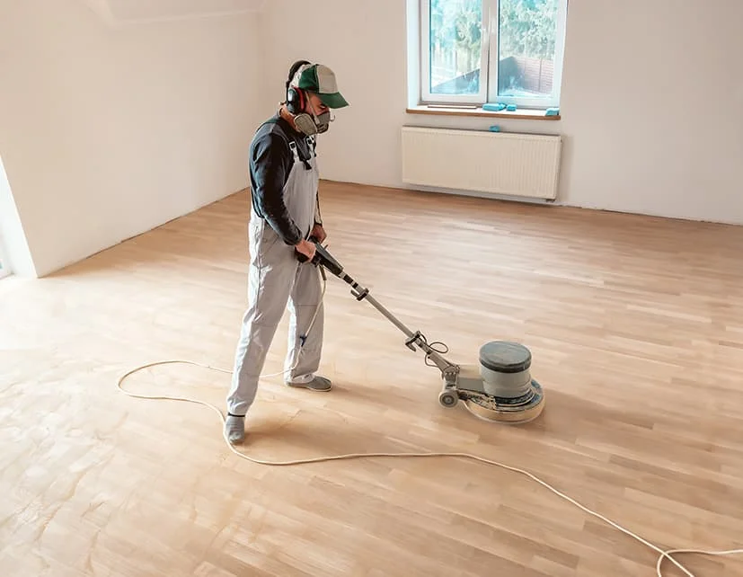 Profesional realizando el acuchillado y barnizado de parquet en Madrid con maquinaria especializada sin polvo en una habitación vacía